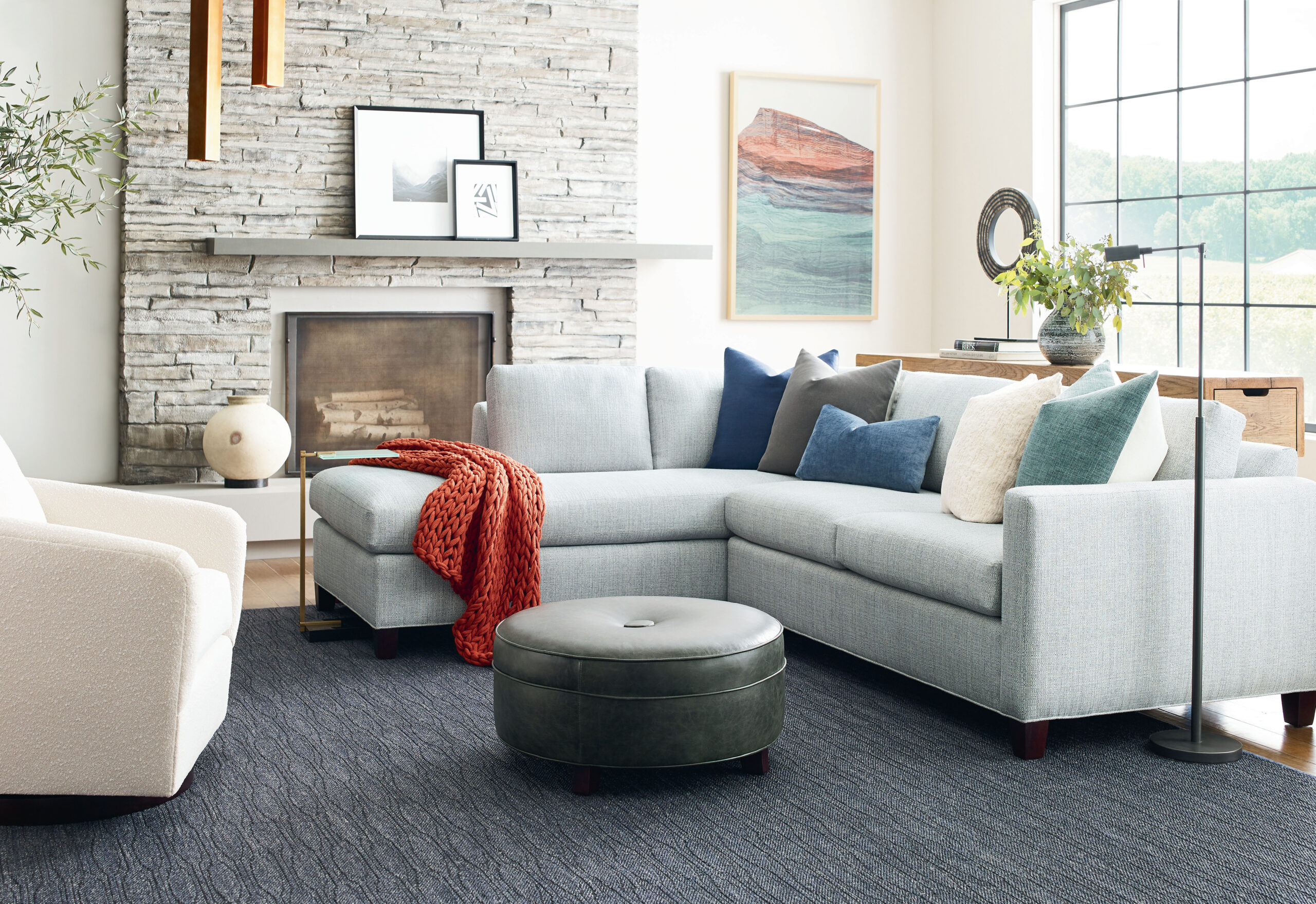 Bright living room with blue sectional sofa, fireplace with grey stonework, modern lamp, and colorful artwork