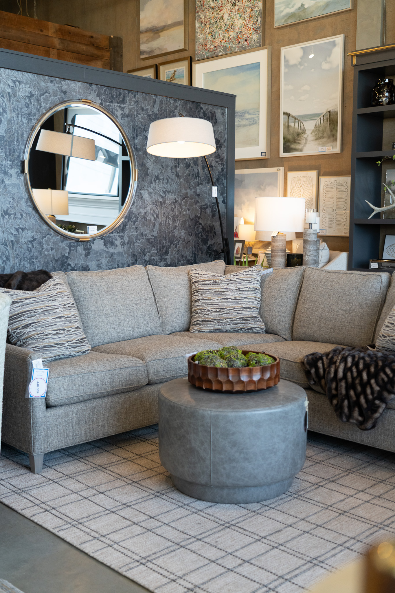 Furniture showroom with grey sofa, ottoman, and circular mirror
